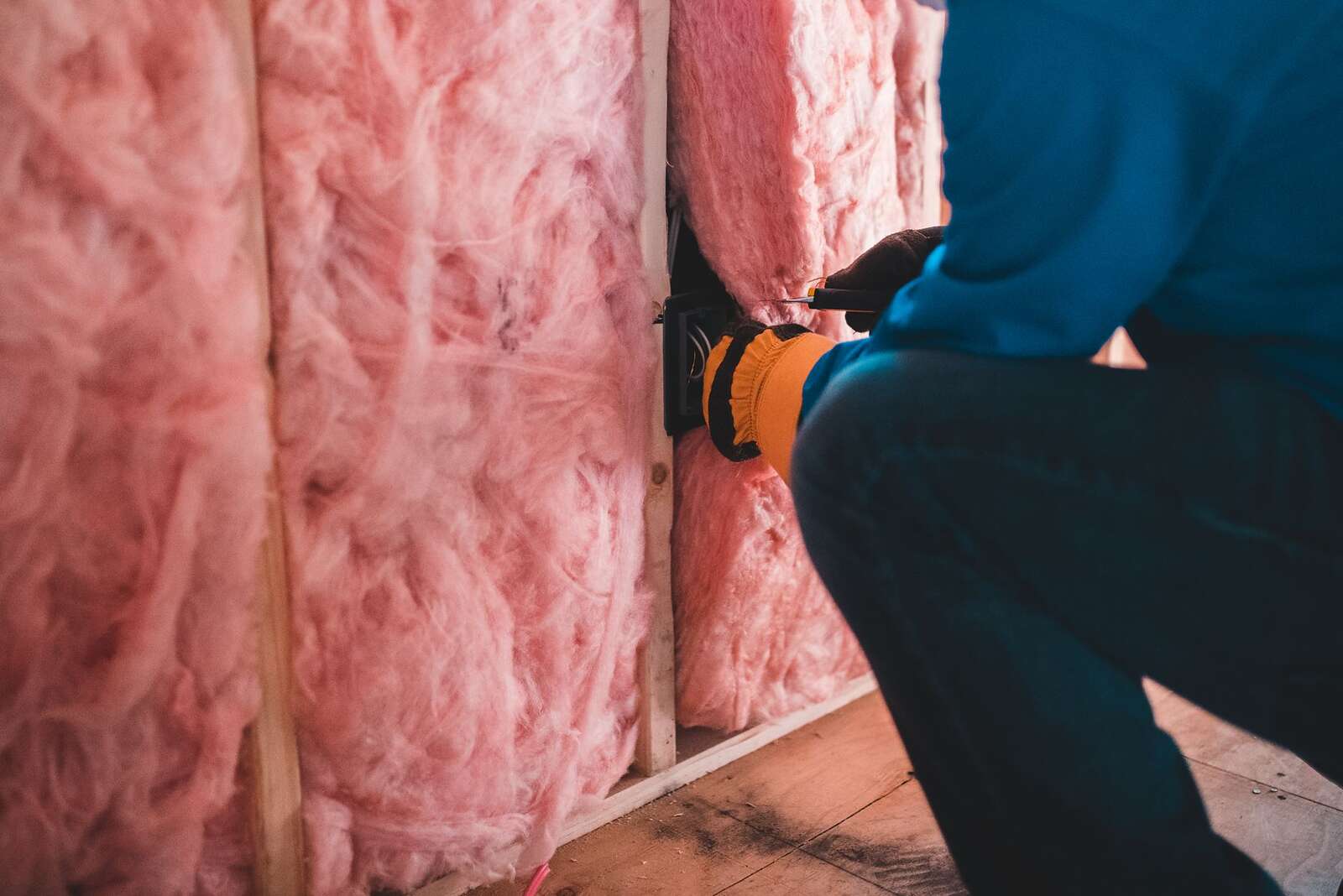 A gloved worker crouched beside insulation batts, face out of frame