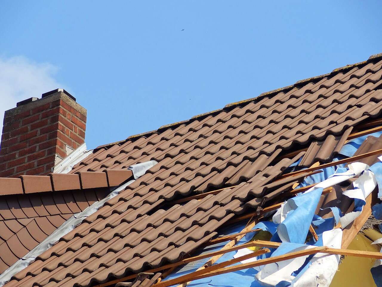 A house roof with tiles torn off and debris in the yard after a hurricane