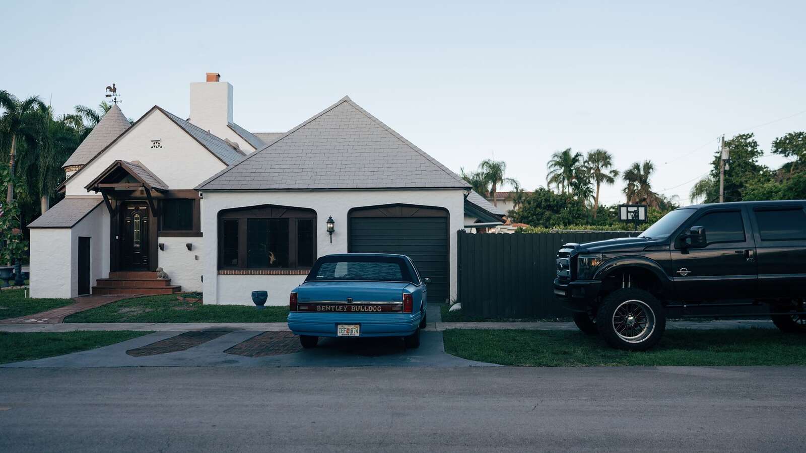 A mid-century single-story house with a low roofline, a driveway and mature planting